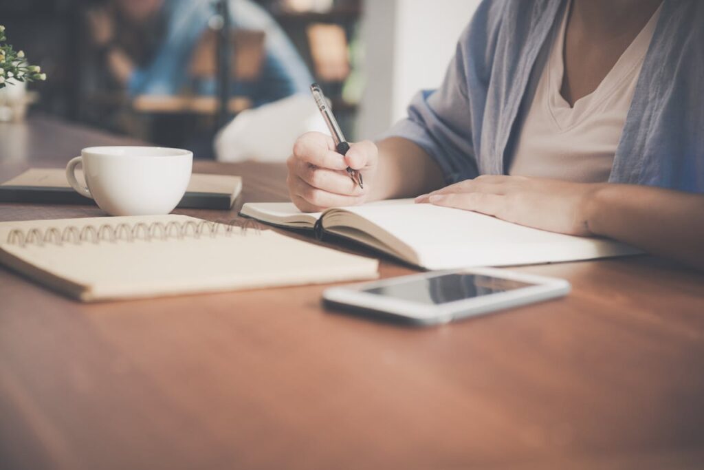 Mujer escribiendo en un cuaderno junto a una taza de té y un ordenador Tablet